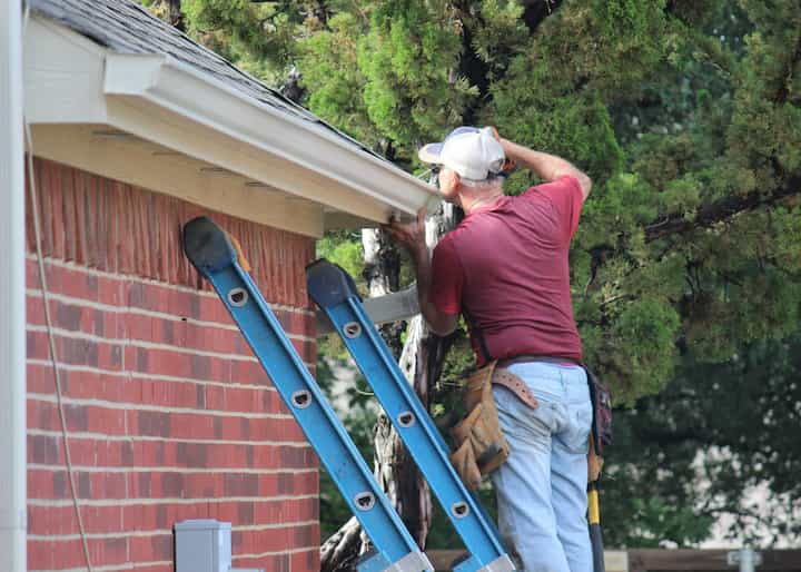 A professional roofing repair expert wearing jeans on ladder in Victorville, California